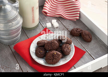 Rustico cacao Biscotti e pistacchi sul vassoio in legno con una bottiglia di latte, zuccheriera alluminio, pistacchi freschi, cubetti di zucchero e tovaglia con striping Foto Stock