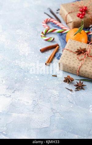 I mandarini freschi con foglie, candy canes, confezioni regalo in carta kraft e spezie - cannella, anice e chiodi di garofano su uno sfondo blu Foto Stock