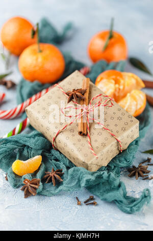 I mandarini freschi con foglie, candy canes, confezioni regalo in carta kraft e spezie - cannella, anice e chiodi di garofano su uno sfondo blu Foto Stock