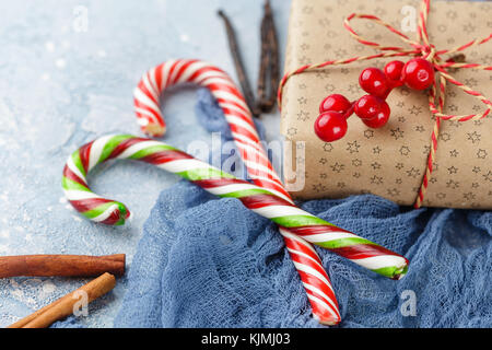 I mandarini freschi con foglie, candy canes, confezioni regalo in carta kraft e spezie - cannella, anice e chiodi di garofano su uno sfondo blu Foto Stock