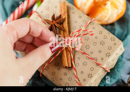 I mandarini freschi con foglie, candy canes, confezioni regalo in carta kraft e spezie - cannella, anice e chiodi di garofano su uno sfondo blu Foto Stock