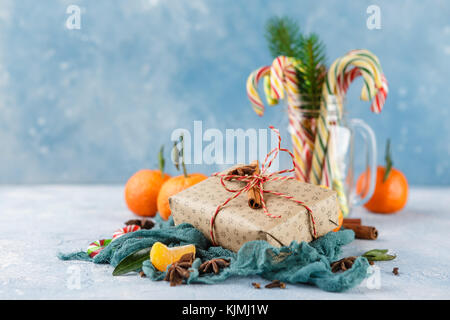 I mandarini freschi con foglie, candy canes, confezioni regalo in carta kraft e spezie - cannella, anice e chiodi di garofano su uno sfondo blu Foto Stock