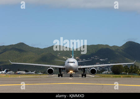 Un Airbus A330-243, rullaggio lungo la pista di decollo e di atterraggio. Vista dalla parte anteriore del velivolo, con colline dietro Foto Stock