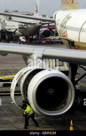 Una Rolls-Royce Trento 772B-60 motore su un Gulf Air Airbus A330-200 ispezionata da uomini che indossano il giallo ad alta viz tabards durante la sosta in corrispondenza del terminale3 wit Foto Stock