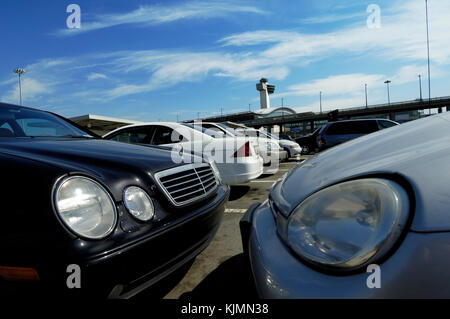 Autovetture private parcheggiato in aeroporto parcheggio auto con il terminale e il controllo del traffico aereo a torre dietro. Foto Stock