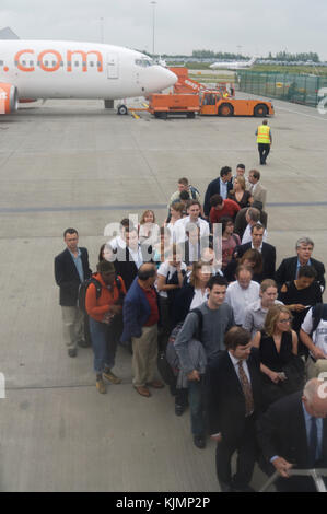 Imprenditori e altri uomini e donne di passeggeri in attesa in una coda sul piazzale di sosta a bordo della 737 tramite il airstairs per il volo EZY2552 con bagaglio a mano Foto Stock