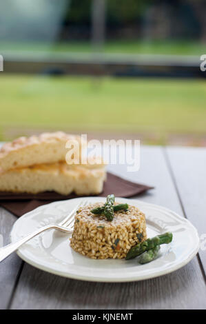 Risotto con asparagi con la piastra di ceramica su tavolo in legno con argento forcella. in background sale di due pezzi di focaccia Foto Stock