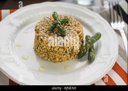 Risotto agli asparagi in piastra ceramica sul tavolo in legno con argento e forcella a strisce colorate tovaglia Foto Stock