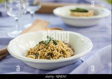 Risotto agli asparagi in due vaso di ceramica sulla tovaglia viola con una forcella di argento e bicchieri in background Foto Stock