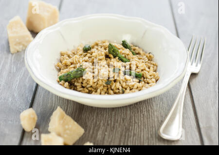 Asparagi risotto in piastra ceramica sul tavolo di legno con forcella di argento e pezzi di formaggio parmigiano Foto Stock