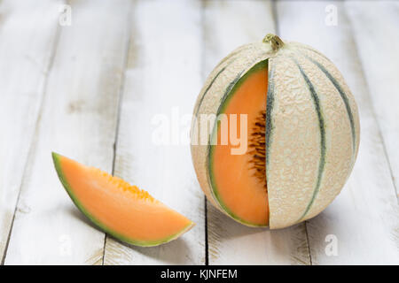 Il miele melone tagliata aperta sul bianco sullo sfondo di legno. Foto Stock