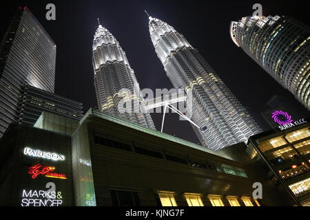 Le Petronas Twin Towers di Kuala Lumpur tra due altri grattacieli durante la notte. questo edificio circolare è il monumento più famoso della città Foto Stock