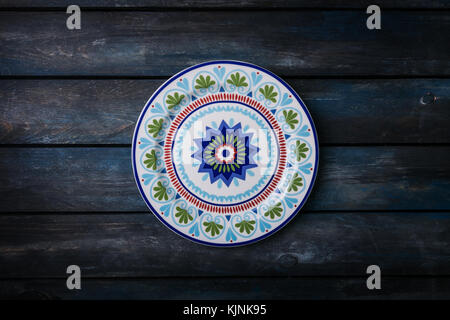 Originale la piastra di ceramica con un bellissimo ornamento colorati. top view scuro dello sfondo in legno Foto Stock