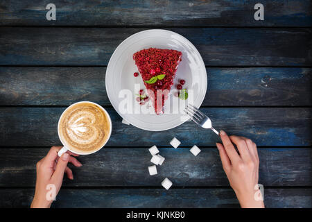 Vista dall'alto. fetta di deliziosa torta rossa del velluto e latte caffè con le mani delle donne e rafinated zucchero su un colore di sfondo di legno Foto Stock