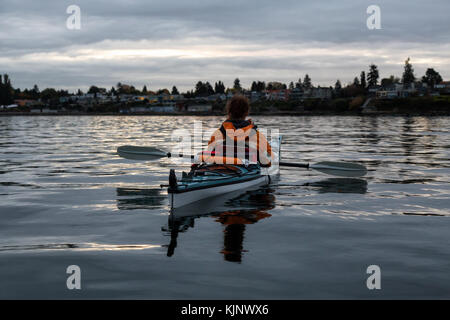 Avventurosa donna è il kayak durante un alba con case residenziali in background. presi in Vancouver, British Columbia, Canada. Foto Stock