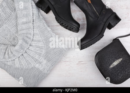 Un set di inverno di moda abbigliamento femminile. maglione di lana, scarpe e borsetta in bianco sullo sfondo di legno. Foto Stock