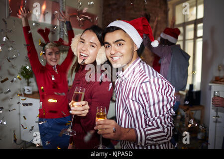 Ragazza estatica e il suo fidanzato con flauti di champagne per divertirti con amici sulla notte di Natale Foto Stock