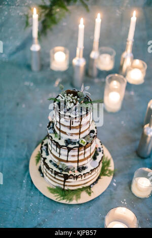 Trattamento, vacanze, dolciumi concetto. gteat tre tier torta di compleanno con foglie e fiori, con frutti di bosco e dolci addobbi, è circondato con un sacco di candele Foto Stock