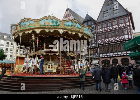 Francoforte, Germania. 28 novembre 2017. Passers-by guarda un vecchio carosello per bambini sulla piazza centrale di Ršmerberg con le vecchie case di Sampastsberg sullo sfondo. Come uno dei più antichi mercatini di Natale in Germania, il mercatino di Natale di Francoforte si tiene ogni anno al tempo dell'Avvento. E' inoltre, con circa 3 milioni di visitatori, uno dei più grandi mercatini di Natale della Germania. Foto Stock