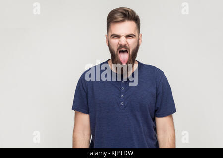 Crazy e concetto di divertimento. barbuto giovane uomo adulto che mostra la linguetta alla telecamera e hanno una felicità look. studio shot, isolata su uno sfondo grigio Foto Stock
