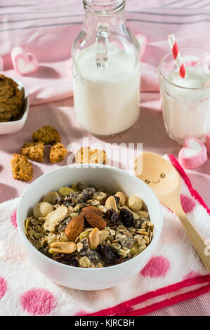 Set colazione. mescolare oat granola in bianco ciotola con cuore rosa dolce marshmallow sulla tabella di sfondo, servire con cookie e bianco latte in vetro e Foto Stock