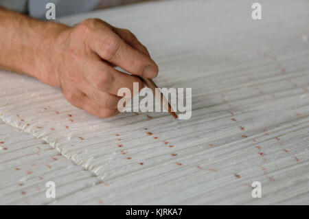 Mano con una matita rende segni sul tappeto. La tessitura e la fabbricazione di tappeti fatti a mano closeup Foto Stock