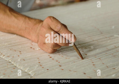 Mano con una matita rende segni sul tappeto. La tessitura e la fabbricazione di tappeti fatti a mano closeup Foto Stock