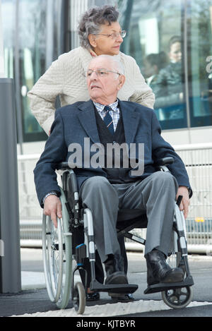 Anziani uomo seduto nella sedia a rotelle spinto da sua moglie Foto Stock
