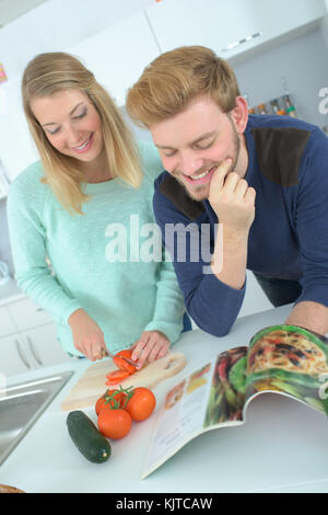 Giovane abbracciando in cucina mentre si verifica il libro delle ricette Foto Stock