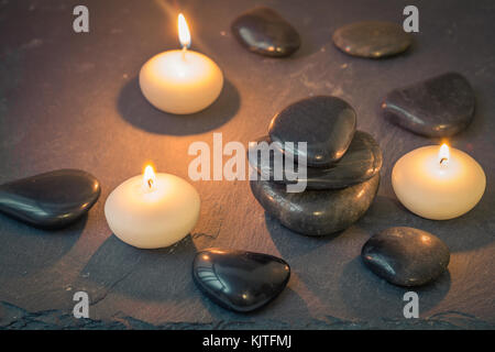 Pietre Nere e candele accese su sfondo scuro Foto Stock