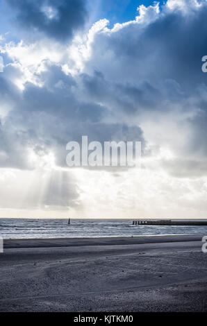 Spiaggia vuota in inverno, con la marea e cieli drammatici, raggi solari provenienti attraverso le nuvole Foto Stock