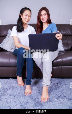 Due giovani donna che utilizza un computer portatile sul divano nel soggiorno di casa Foto Stock