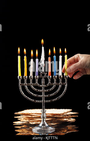 Il menorah con candele accese per hanukkah su uno sfondo nero. matza in background. Foto Stock