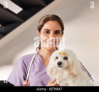 Fiducioso giovane donna ispanica a lavorare come veterinari, felice vet giocando con il cane di casa durante la chiamata. Medico animale visitando malati animale a casa, un sorridente Foto Stock