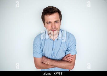 Fiducioso caucasico giovane uomo bello in maglietta blu mantenendo le braccia incrociate e sorridente Foto Stock