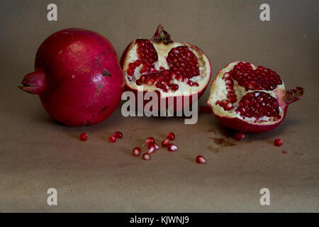 Un intero (intero) e una melagrana frutta tagliata a metà contro sfondo marrone - food still life Foto Stock