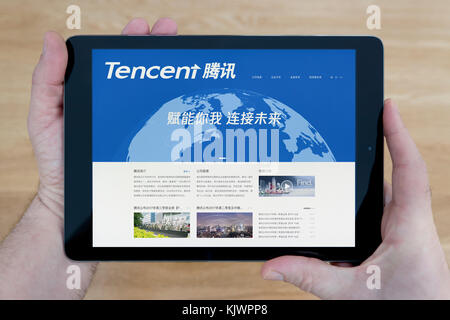 Un uomo guarda la Tencent sito sul suo iPad dispositivo tablet, sparato contro un tavolo di legno top sfondo (solo uso editoriale) Foto Stock