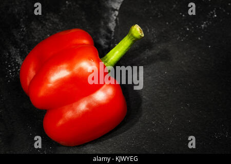 Tagliare a metà il peperone rosso al buio su un sfondo di ardesia, il fuoco selettivo, spazio per il testo. Foto Stock