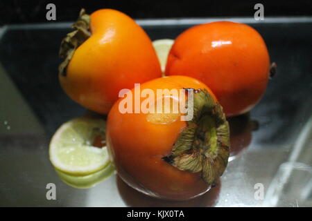 Bella appetitosi dolci colorati persimmon succosa frutta con fette di limone il mix di cocktail Foto Stock