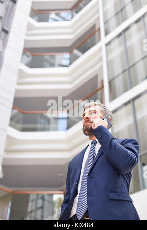 Vita-up verticale di fiduciosa barbuto imprenditore telefono leader i negoziati con i partner aziendali mentre si sta in piedi in spaziosa lobby di office Foto Stock