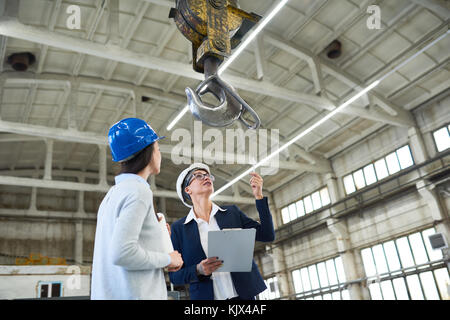 Allegro investitore femmina in hardhat puntando alla gru da cantiere e discutere di edificio con forewoman al sito in costruzione Foto Stock