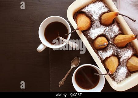 Pane al cioccolato torta con pere intere dentro al forno e due tazze di caffè su sfondo scuro. Vista superiore Foto Stock