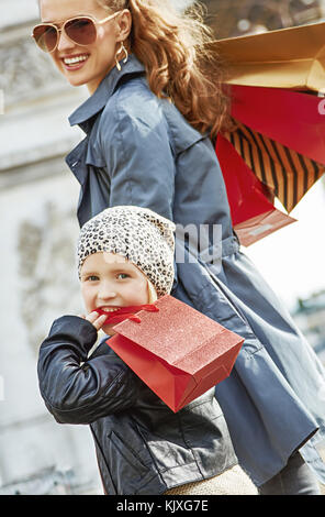 Elegante autunno a Parigi. sorridente giovane madre con bambino e borse per lo shopping nelle vicinanze del Arc de triomphe a Parigi in Francia a piedi Foto Stock