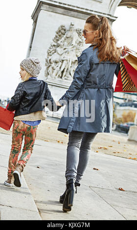 Elegante autunno a Parigi. visto da dietro a piena lunghezza Ritratto di felice giovane madre con bambino e borse per lo shopping in Parigi, Francia cercando riposo e Foto Stock
