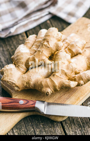 Un sano di radice di zenzero su un tagliere giacente su un vecchio tavolo in legno. Il concetto di cibo. Foto Stock