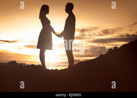 Sillhouette di una coppia in amore tenendo le mani sulla collina al tramonto Foto Stock