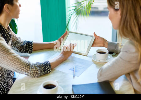 Angolo di alta vista di due moderni irriconoscibili le donne con lavoro a tavola in cafe con tavoletta digitale durante la riunione di affari Foto Stock