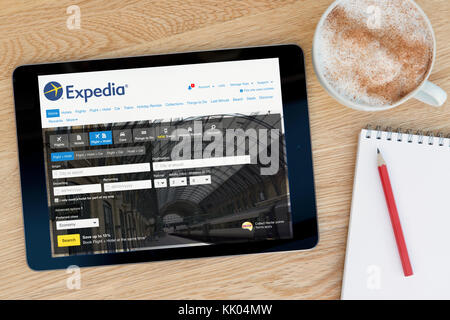 Un uomo guarda il sito di Expedia sul suo iPad dispositivo tablet, sparato contro un tavolo di legno top sfondo (solo uso editoriale) Foto Stock