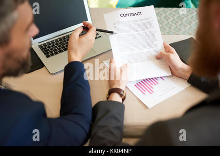 Sulla spalla di un irriconoscibile business partner seduto alla scrivania in ufficio mentre per discutere i dettagli del contratto prima della firma di esso Foto Stock