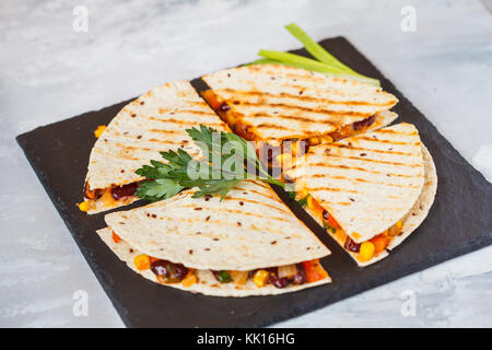 Pezzi di quesadilla con verdure e formaggio su ardesia, sfondo luminoso. vegetariano mangiare sano concetto. Foto Stock